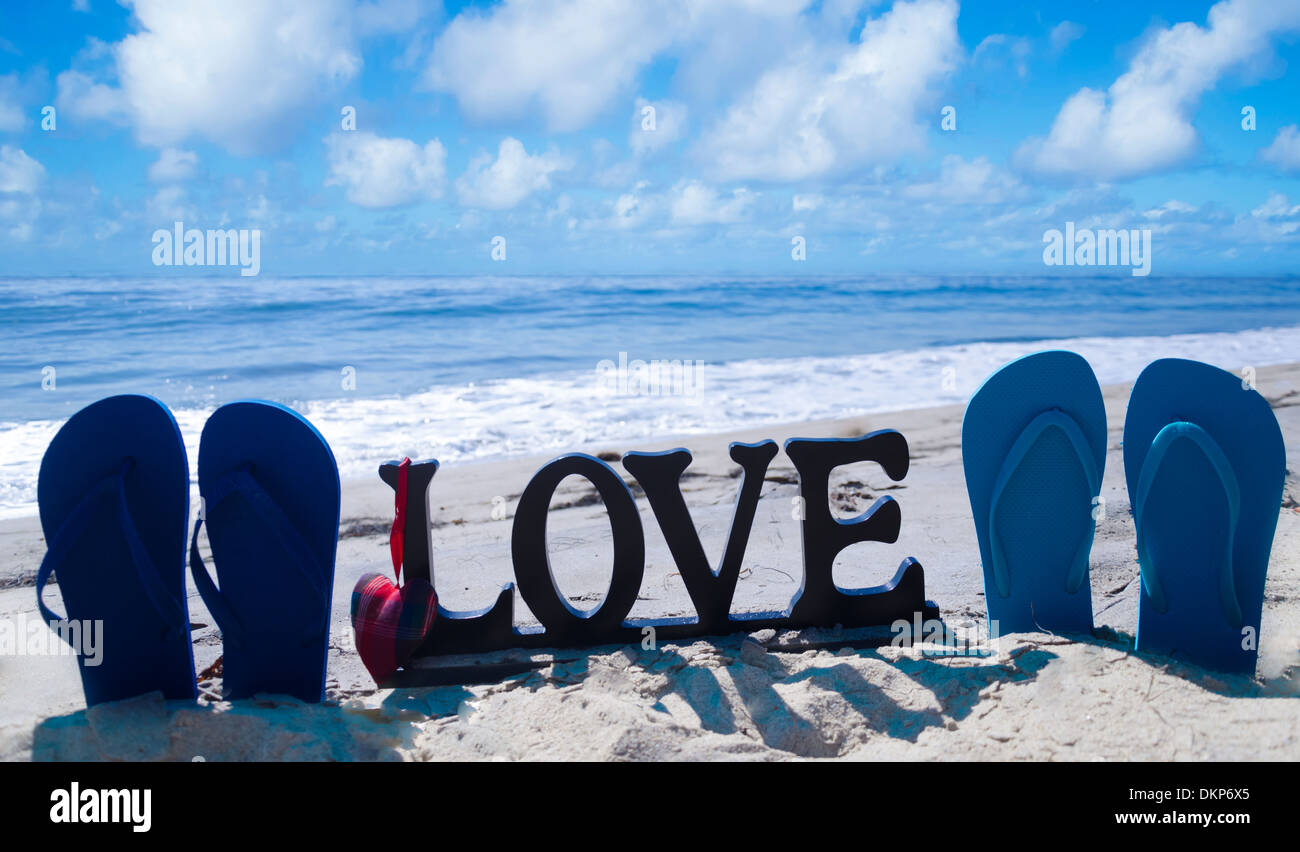 Il flip flop con segno 'amore' e il cuore sulla spiaggia sabbiosa dall'oceano Foto Stock