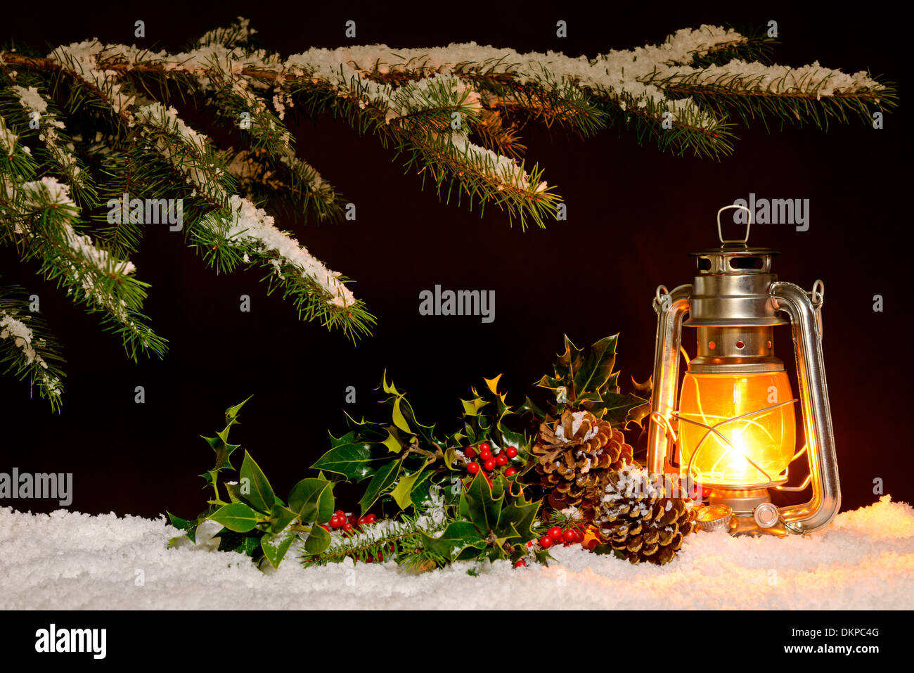 Scena di natale - un olio riempito di masterizzazione lanterna luminosa con coperta di neve albero, agrifoglio ed edera illuminato dalla luce della lampada. Foto Stock