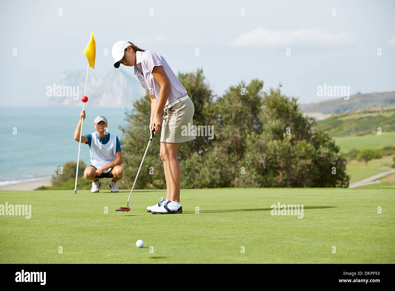 Caddy guardando la donna putt sul campo da golf Foto Stock