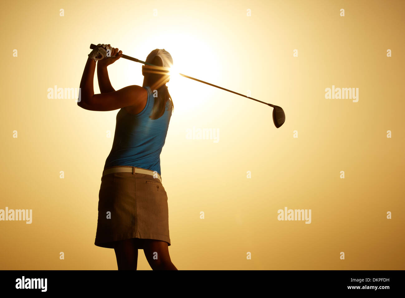 Sole che splende dietro donna swinging golf club Foto Stock
