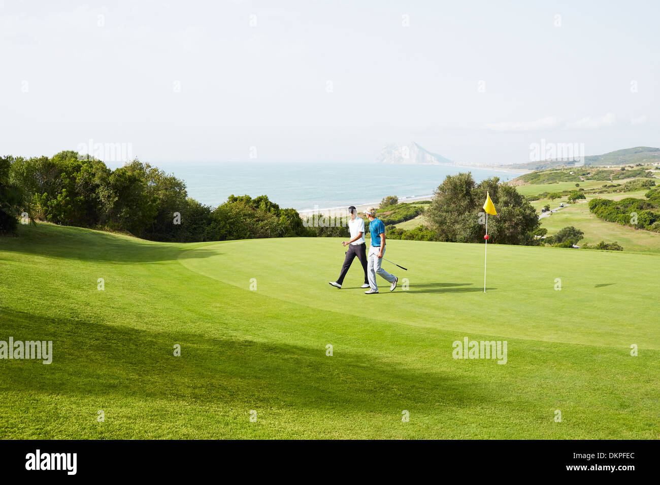 Gli uomini camminare sul campo da golf con vista sull'oceano Foto Stock
