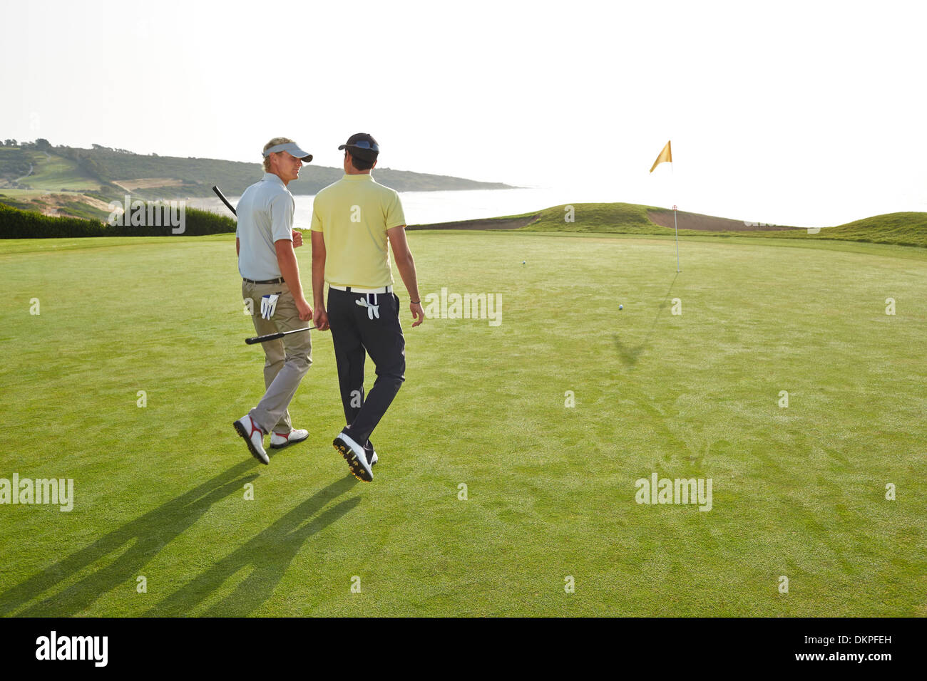 Gli uomini a camminare verso il foro sul campo da golf con vista sull'oceano Foto Stock