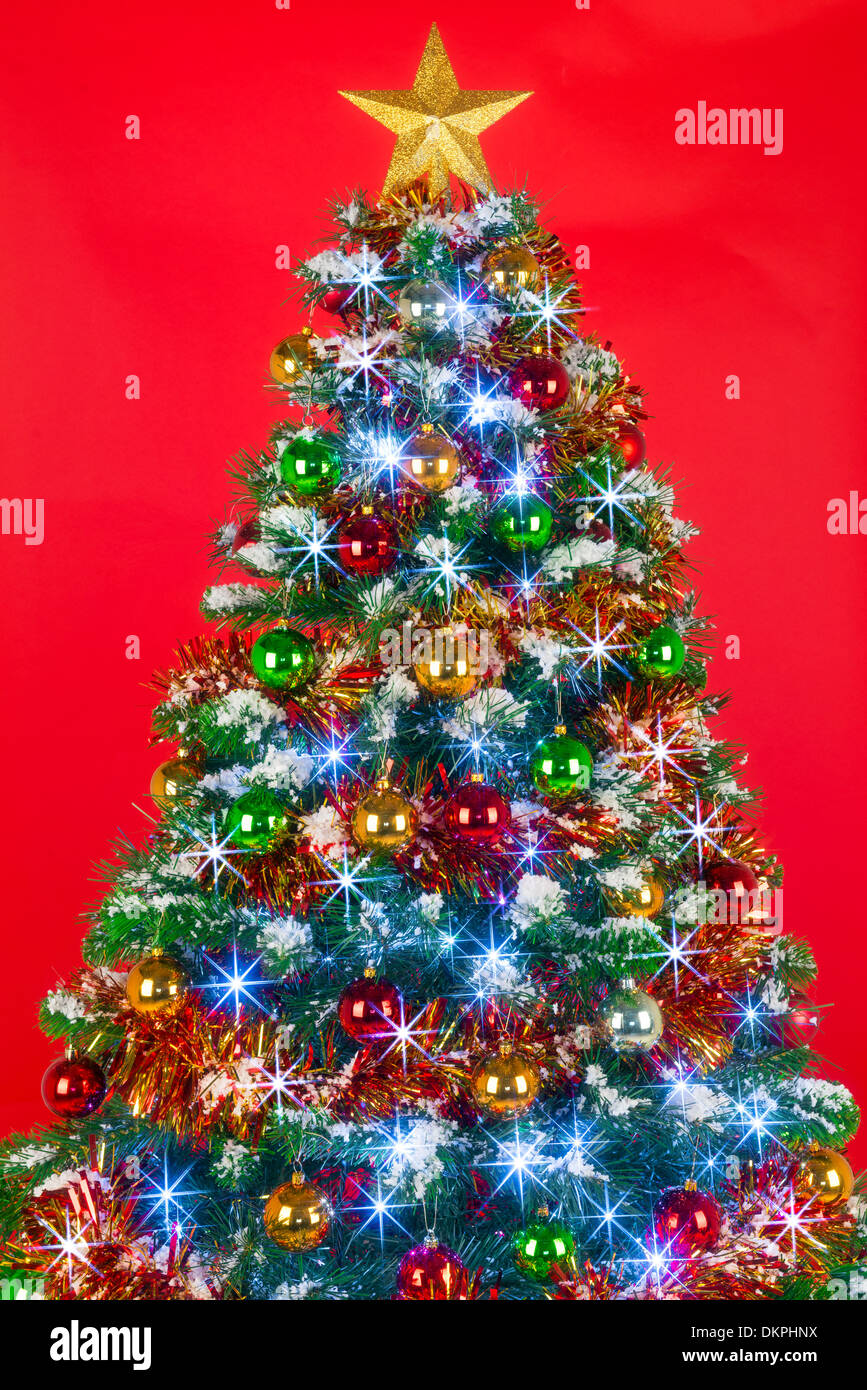 Un albero di Natale decorato con baubles, tinsel e luci fairy contro uno sfondo di colore rosso. Foto Stock