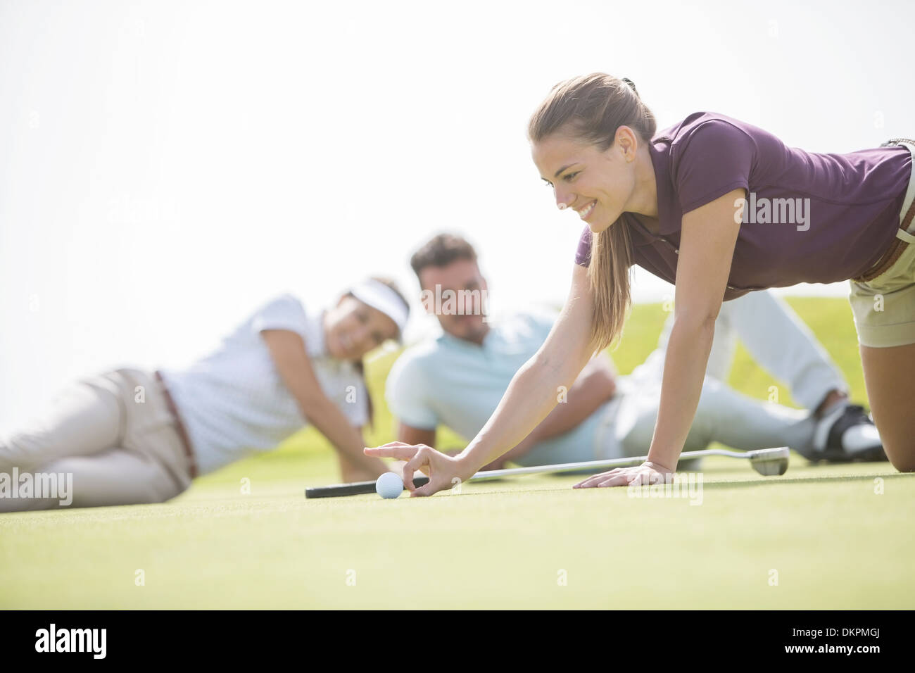 Gli amici a guardare la donna sfiora la pallina da golf verso il foro Foto Stock