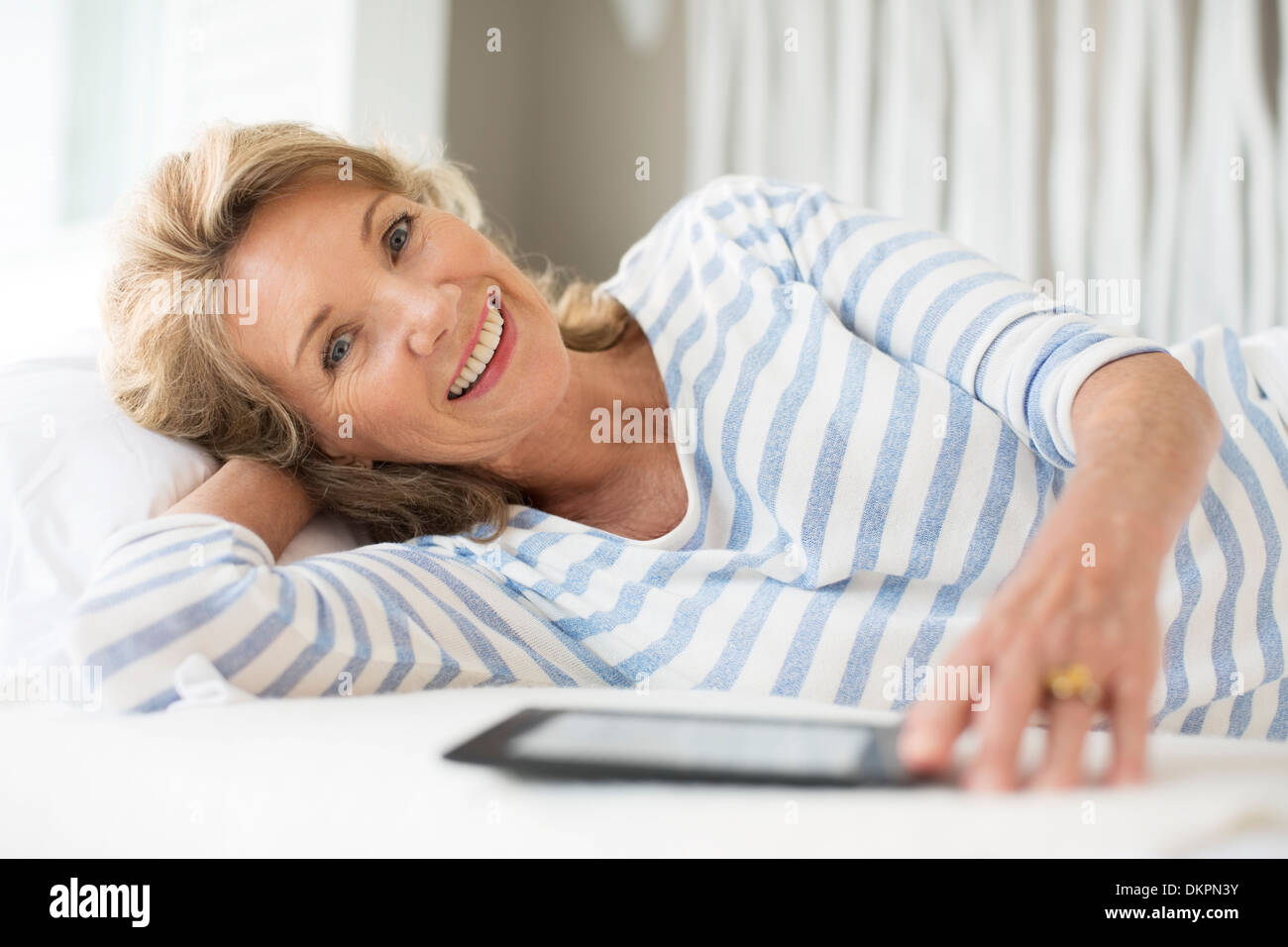 Donna anziana con tavoletta digitale sul letto Foto Stock