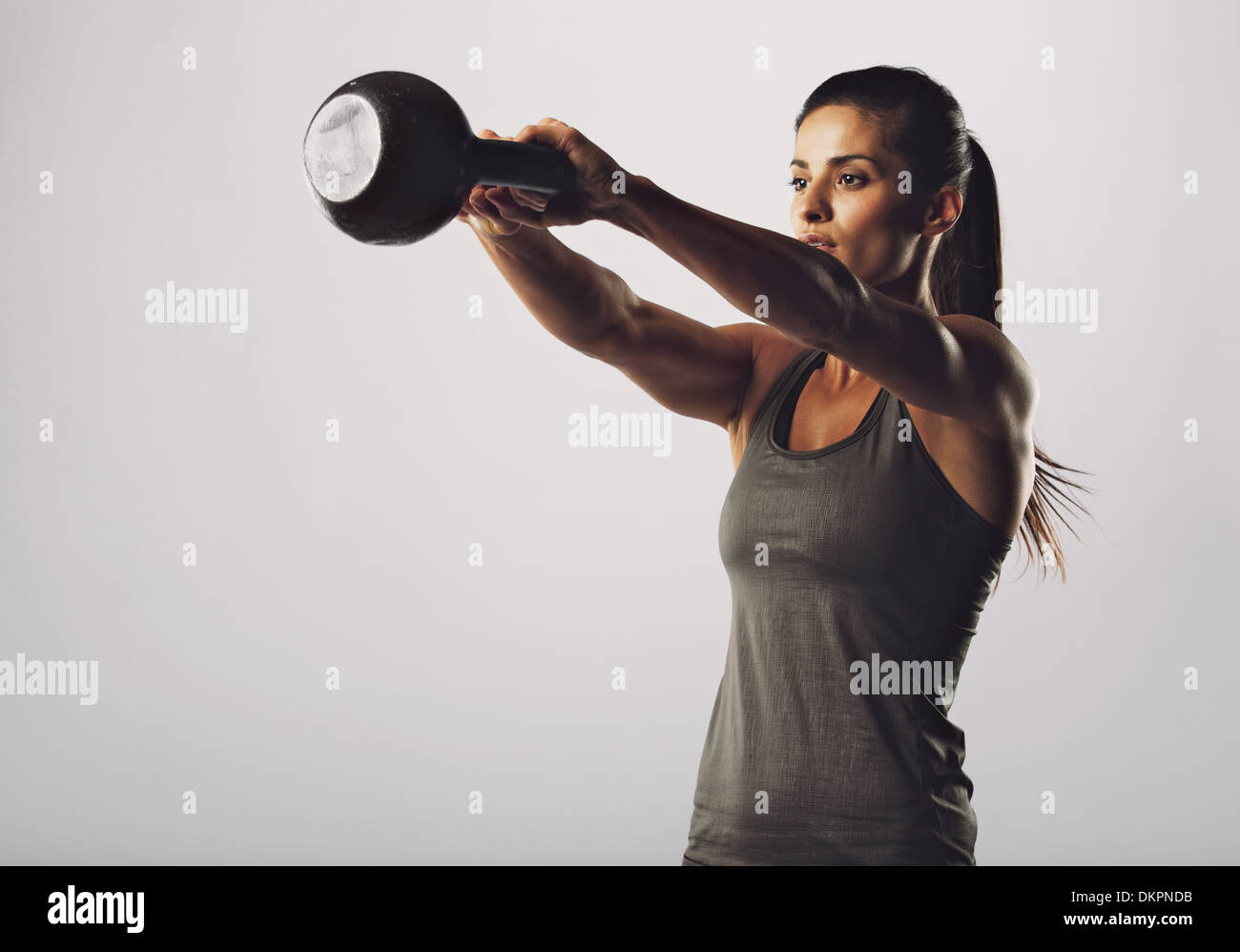 Immagine del giovane attraente femmina bollitore facendo esercizio di campana su sfondo grigio. Donna Fitness lavoro fuori. Esercizio Crossfit. Foto Stock