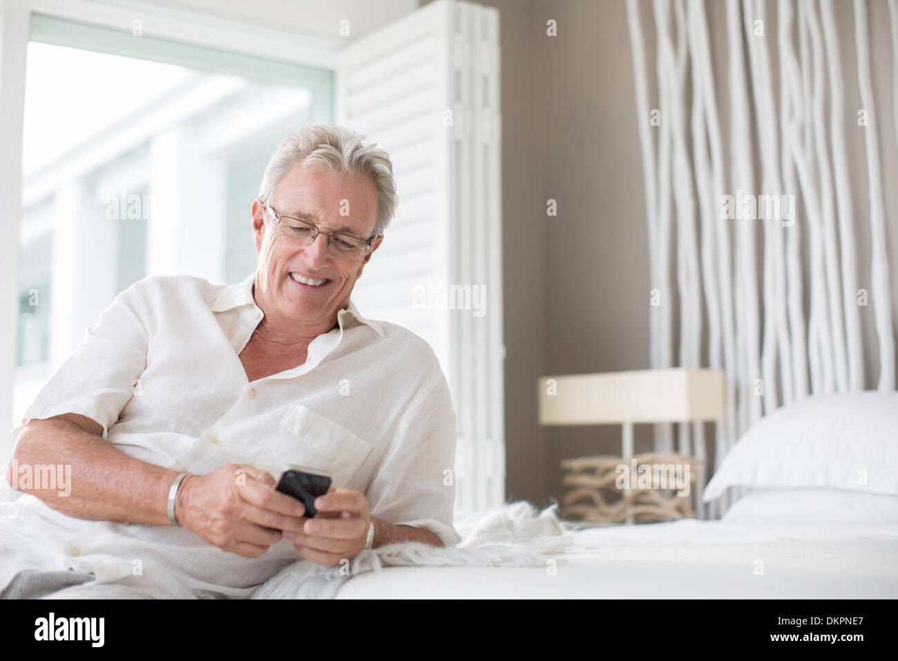 Uomo anziano tramite telefono cellulare sul letto Foto Stock