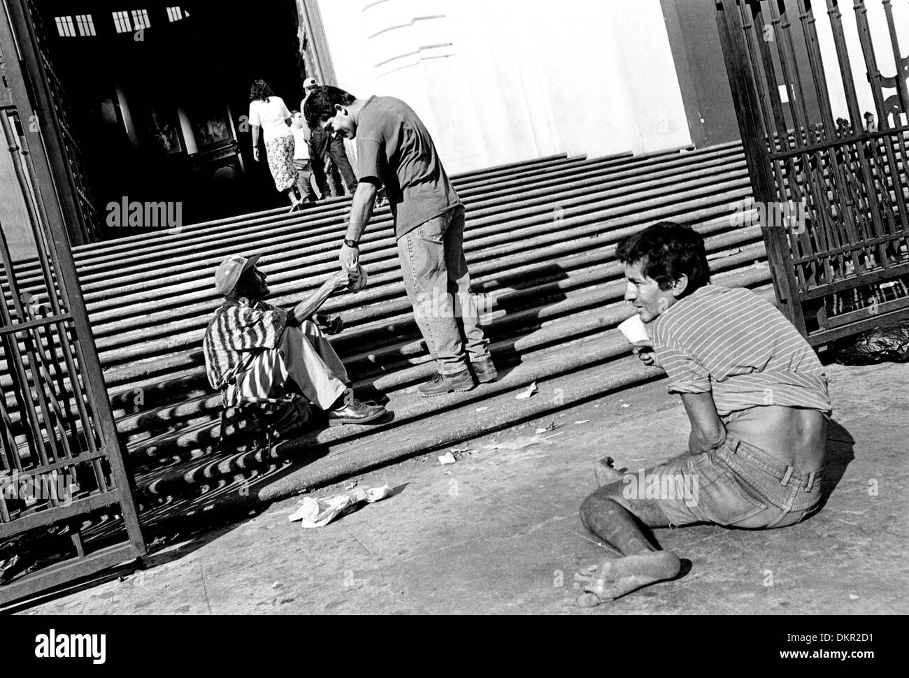 Nov. 19, 2002 - San Salvador El Salvador - al di fuori della cattedrale di San Salvador, Jesse Villalta, di Long Island, New York, si ferma a dare soldi ai mendicanti il cui sacco nella vita non è cambiato molto in quanto il 1980 assassinio dell Arcivescovo Oscar Romero, che ha sostenuto la causa dei poveri e fu ucciso per esso. (Credito Immagine: © Benjamin Rusnak/ZUMAPRESS.com) Foto Stock