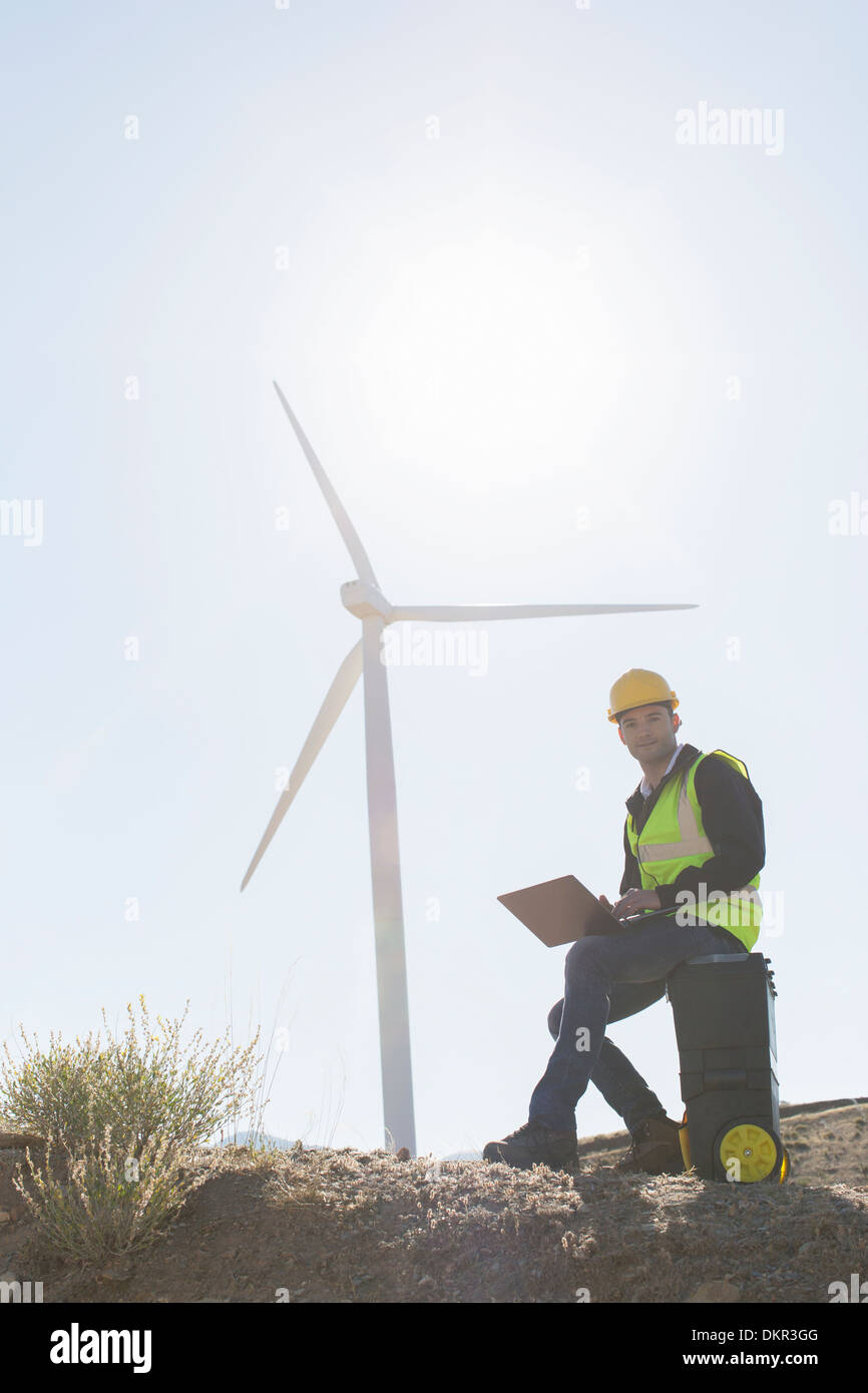 Lavoratore utilizzando laptop dalla turbina eolica nel paesaggio rurale Foto Stock