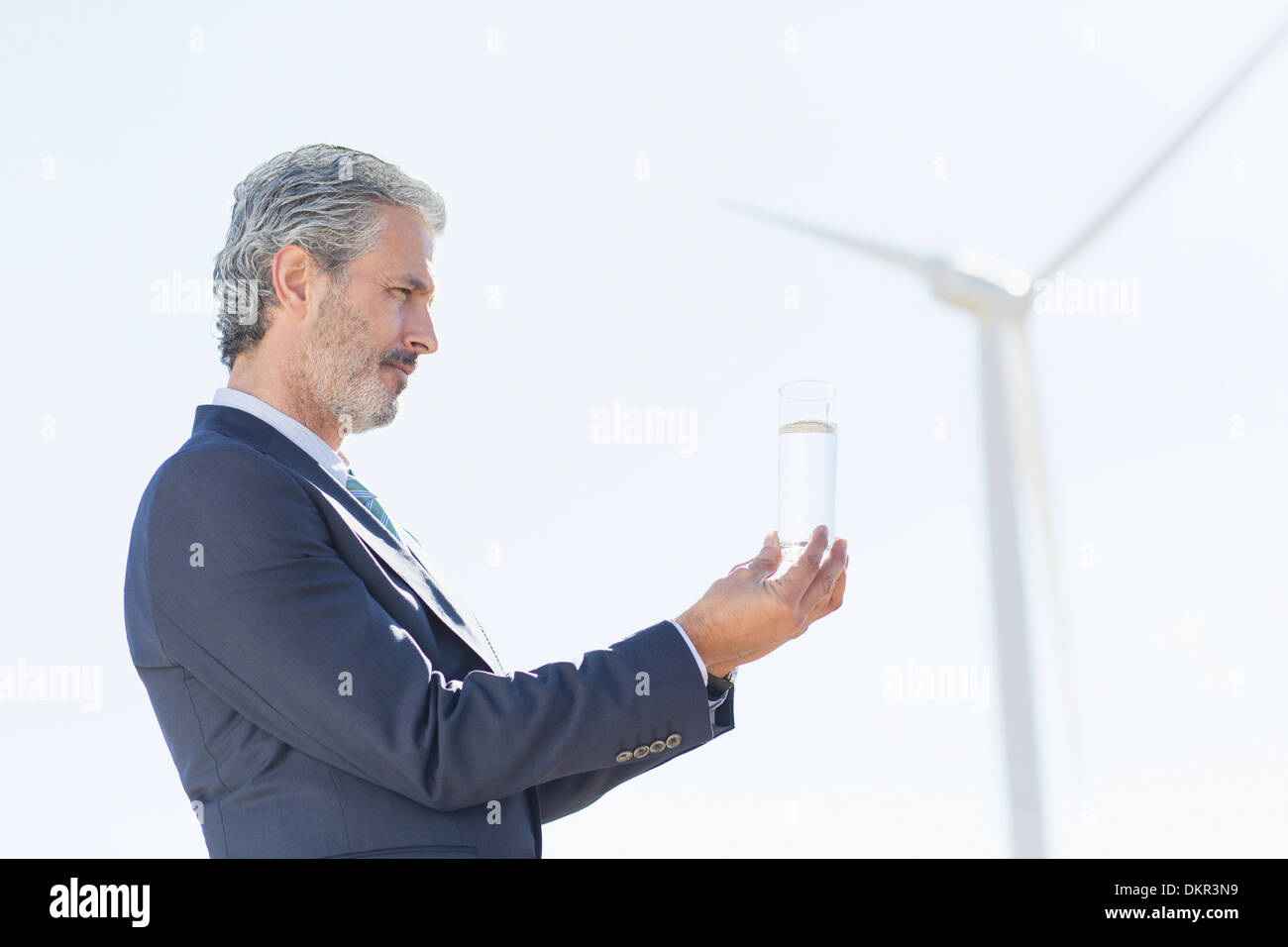 Imprenditore esaminando un bicchiere di acqua mediante la turbina eolica Foto Stock