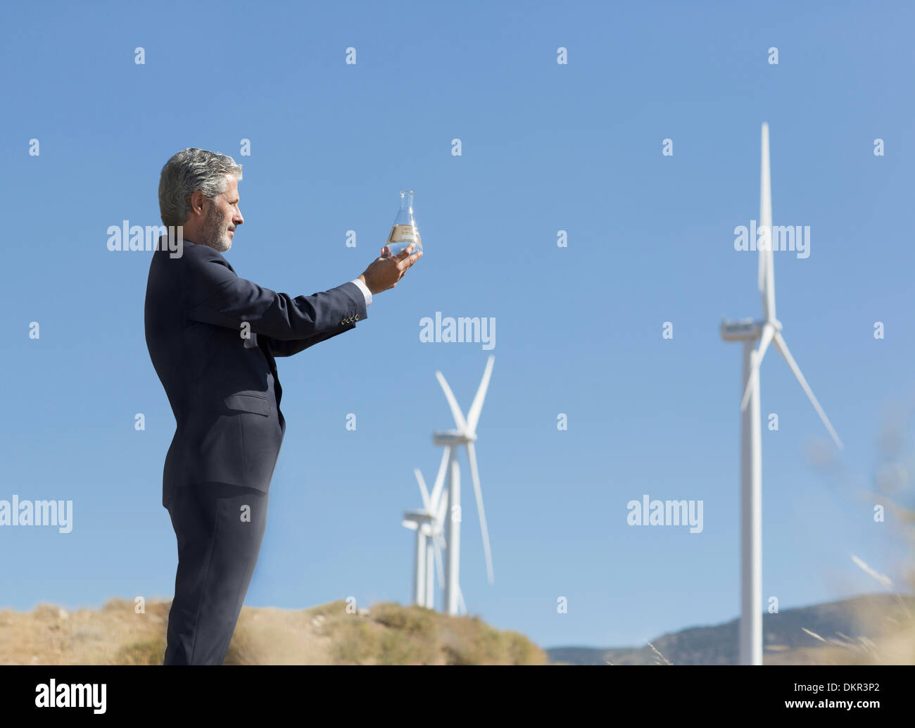 Imprenditore con un bicchiere di acqua da turbine eoliche nel paesaggio rurale Foto Stock