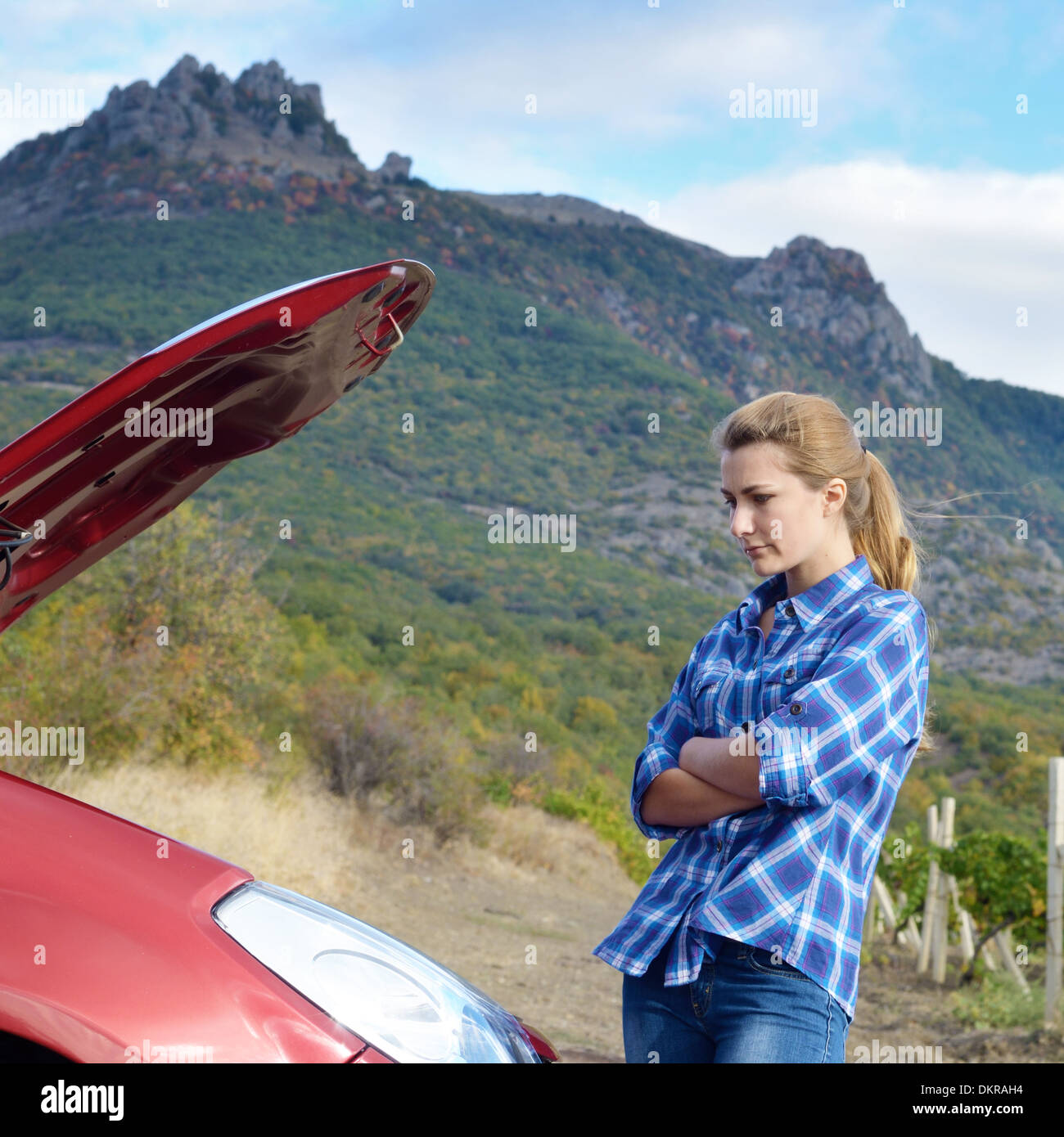 Giovane donna vicino a Broken auto richiede assistenza per guardare sotto il cofano aperto Foto Stock