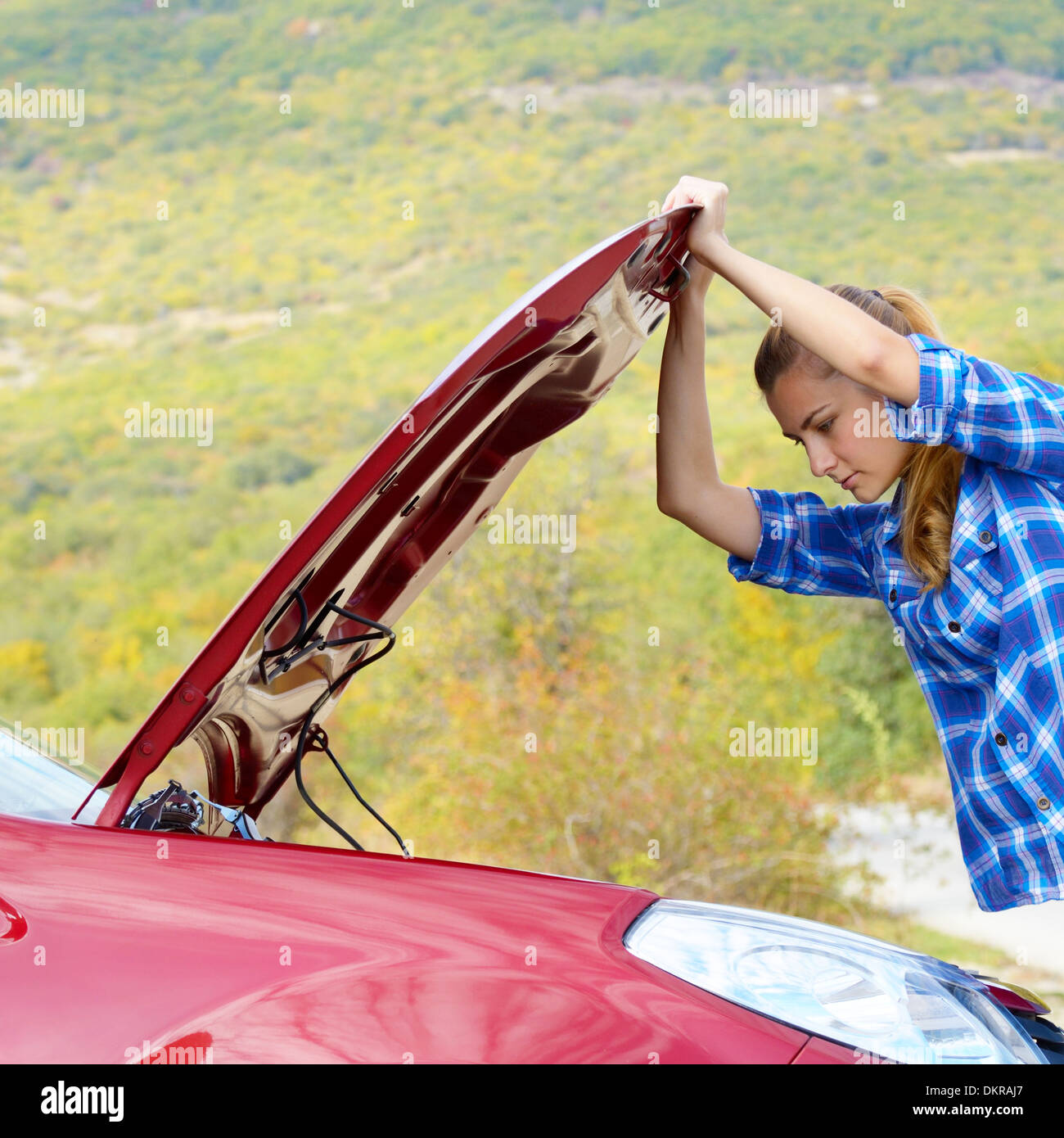 Giovane donna vicino a Broken auto richiede assistenza per guardare sotto il cofano aperto Foto Stock