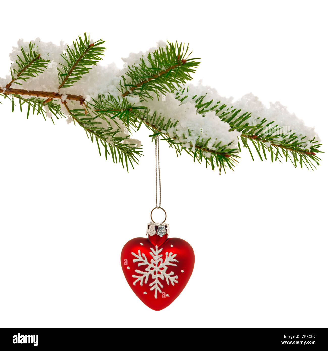 Rosso a forma di cuore ad ornamento di Natale appeso al ramo di un albero di Natale coperto di neve, isolato su uno sfondo bianco. Foto Stock