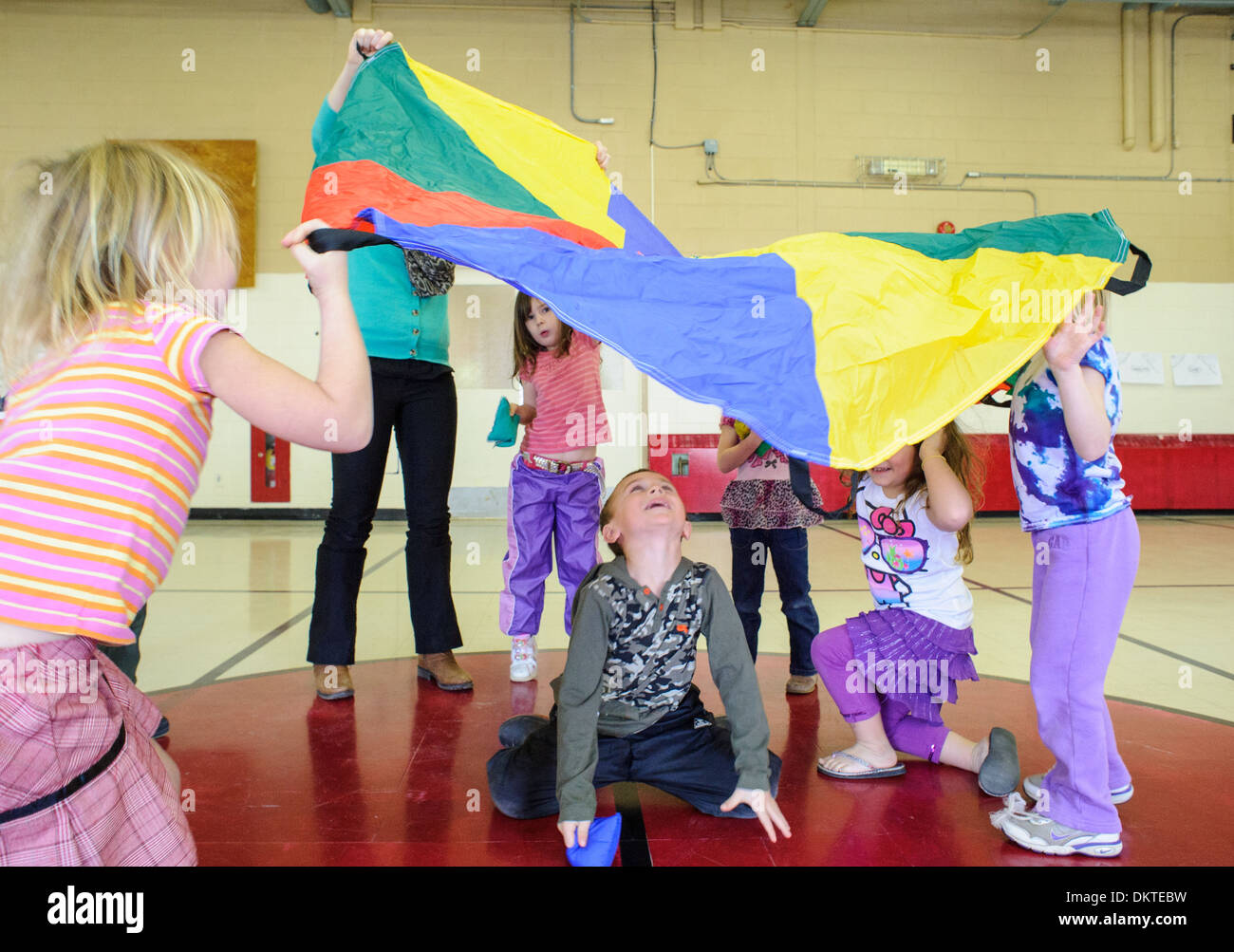 Pre-scuola dei bambini che giocano con il paracadute arcobaleno in palestra Foto Stock