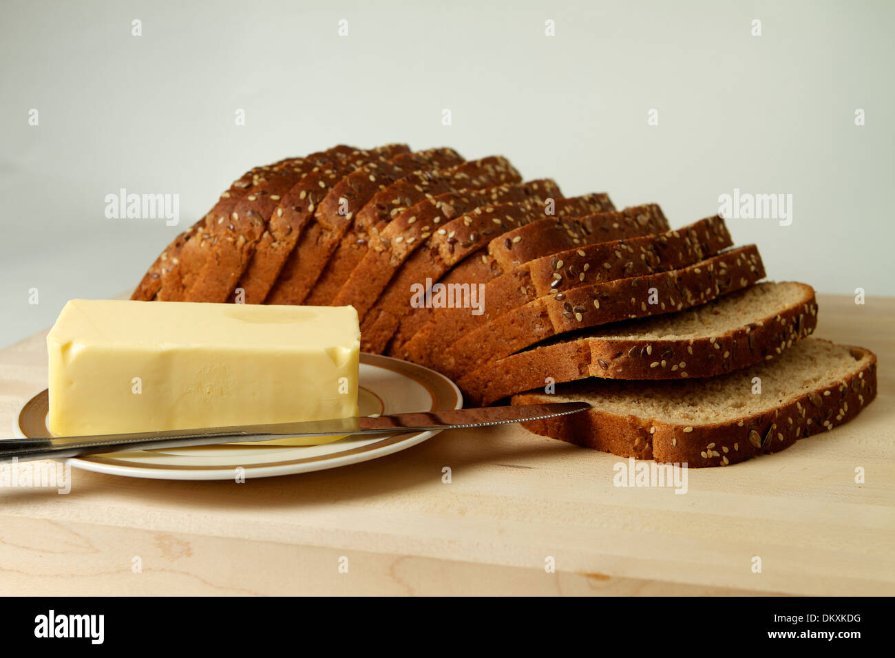 Un multiplo integrale di grano pagnotta di pane su un tagliere di legno con una piastra di burro e un coltello Foto Stock