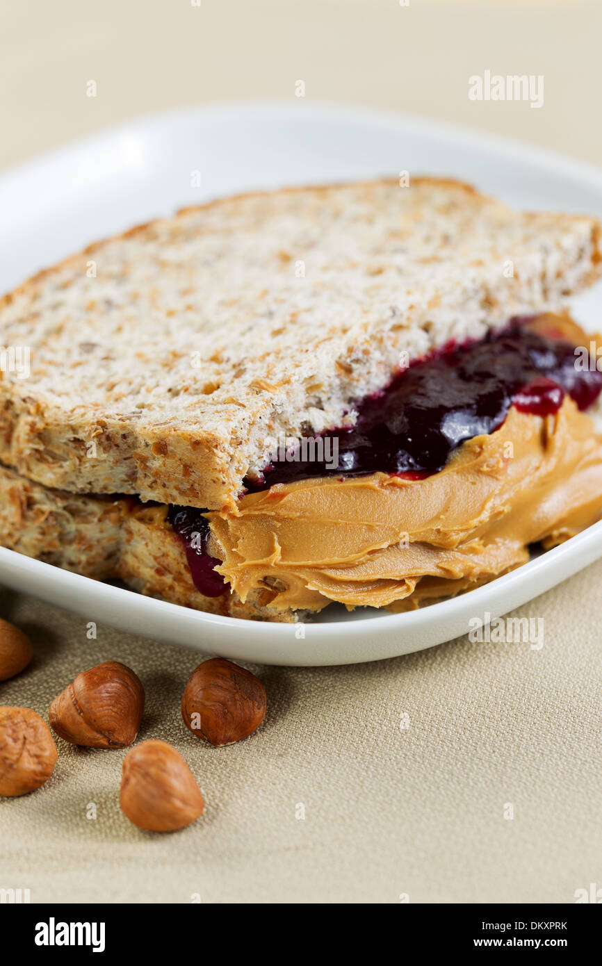 Closeup foto verticale di un burro di arachidi e gelatina panino tagliato a metà, all'interno della piastra bianca con frutti a guscio interi Foto Stock