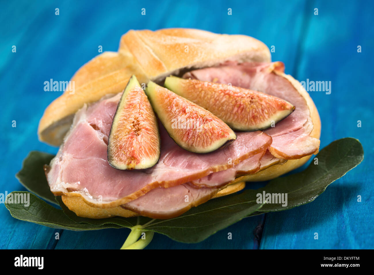 La figura freschi fette di prosciutto affumicato panino sulle foglie di fico su legno blu Foto Stock
