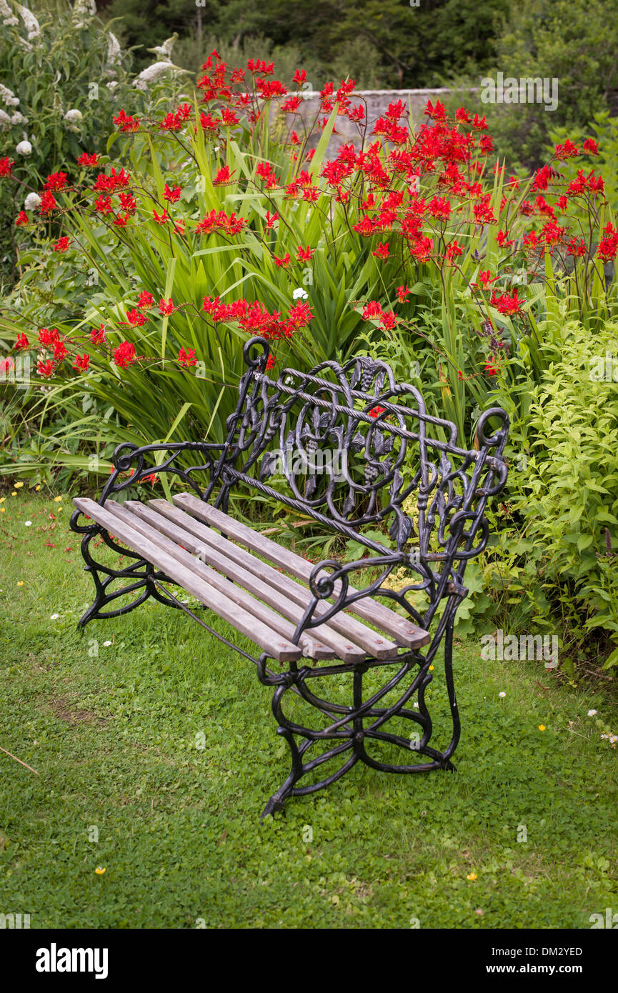 Ornato sedile unico in Applecross giardino con red crocosmia fioritura nelle regioni di frontiera Foto Stock