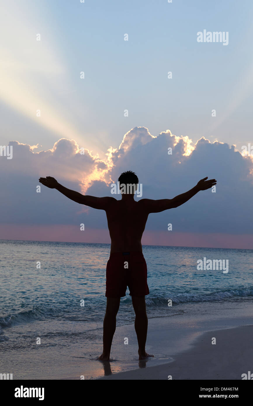 Silhouette di uomo con le braccia tese sulla spiaggia al tramonto Foto Stock