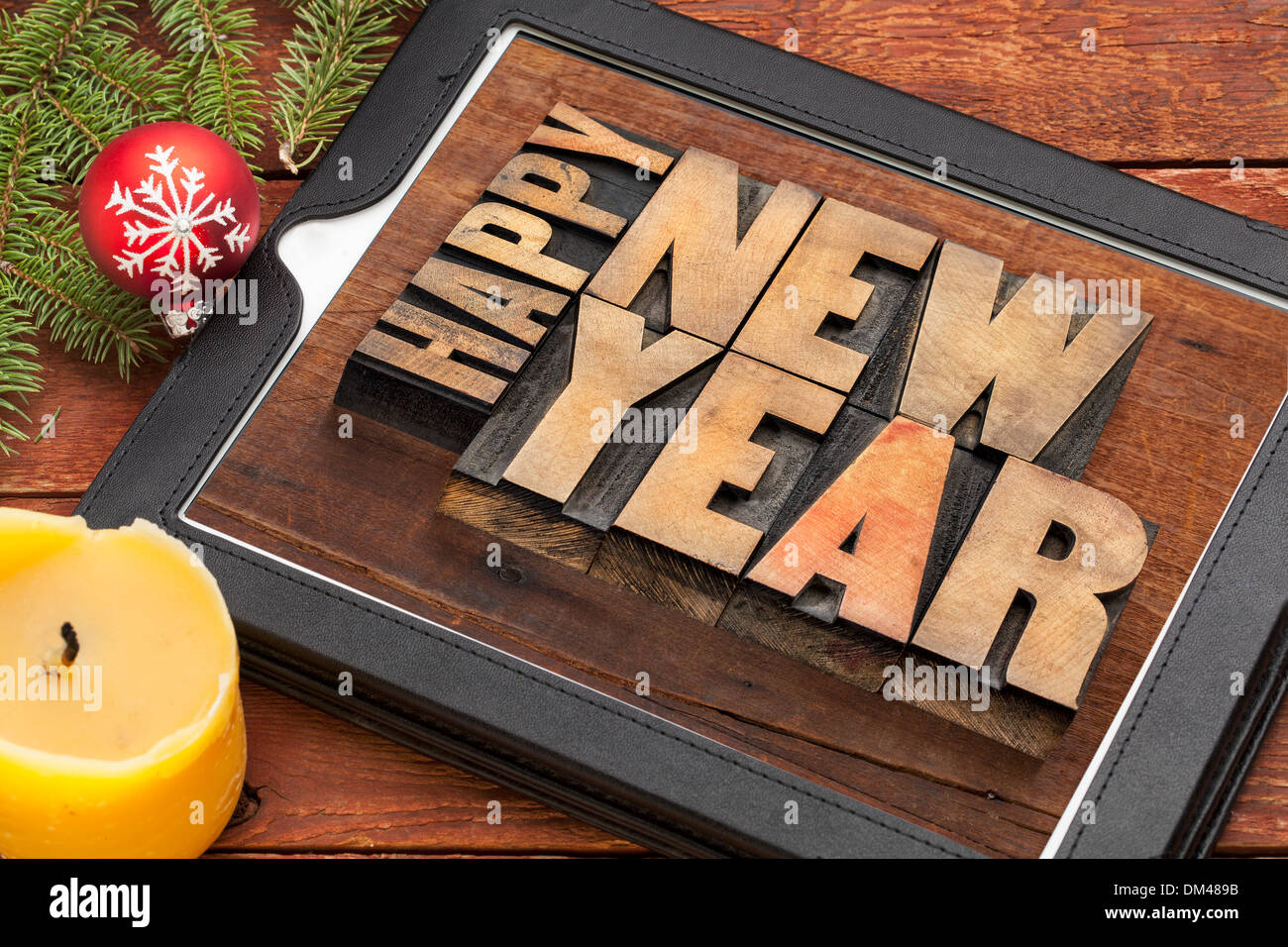 Felice anno nuovo in rilievografia tipo di legno sulla tavoletta digitale computer con una candela e decorazioni Foto Stock