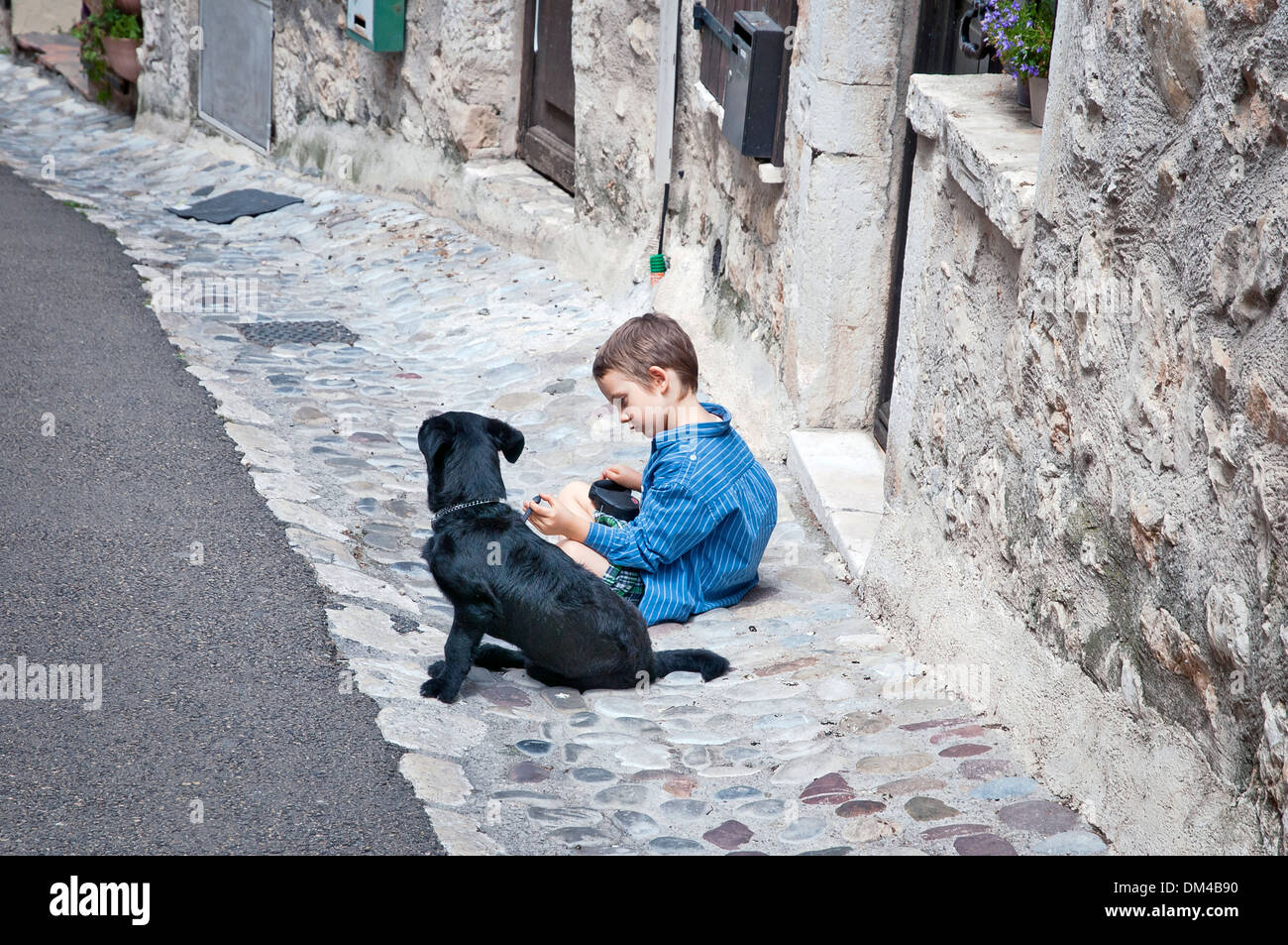 Ragazzo giocando con un cane sulla vecchia strada stretta, Saint-Paul-de-Vence, Francia sudorientale, Riviera Francese, Europa Foto Stock