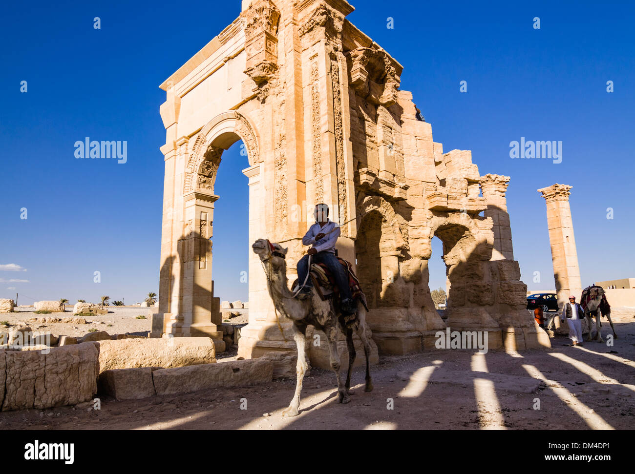 L'uomo sul cammello accanto alla monumentale arco delle rovine di Palmyra, Siria Foto Stock