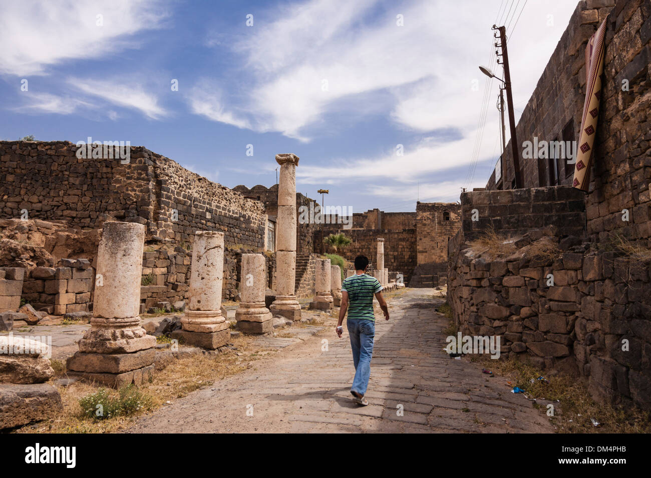 Giovane uomo a piedi attraverso le rovine romane della città vecchia di Bosra, Siria Foto Stock