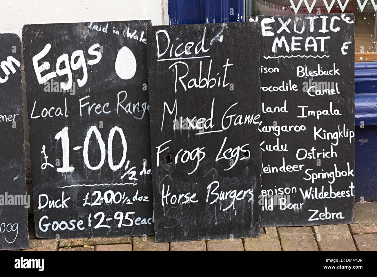 Blackboard segni con carni esotiche e alimenti elencati con i prezzi al di fuori di un negozio di specialità gastronomiche, Abergavenny, Wales, Regno Unito Foto Stock
