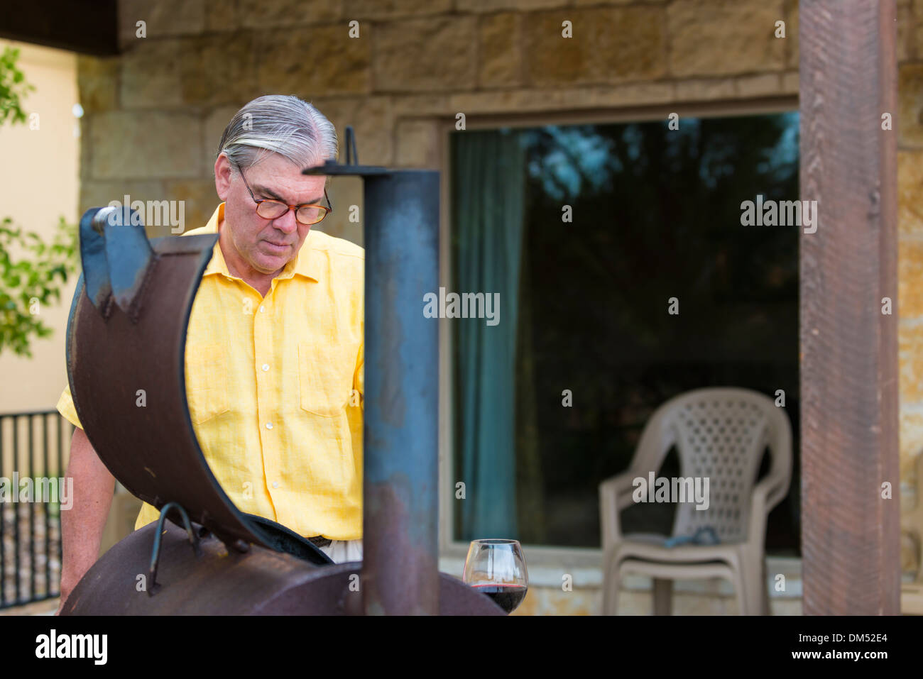 Voce maschile senior citizen di etnia caucasica, 60 anni, sta preparando il barbecue smoker pit per grigliare. Texas, Stati Uniti d'America Foto Stock