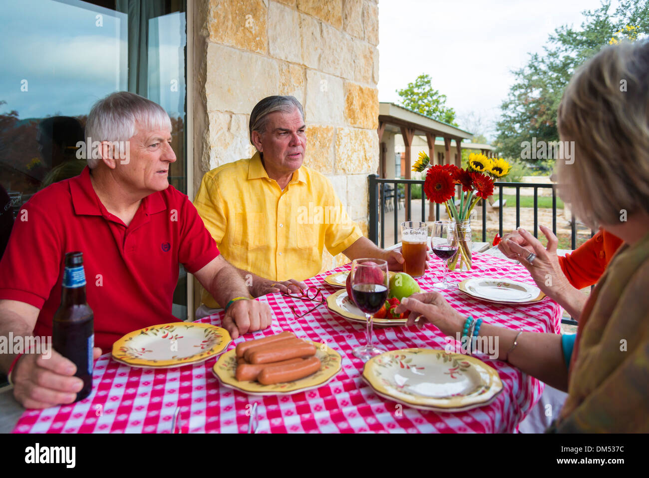 Due coppie di pensionati in un cortile barbecue party. Alimenti e bevande, come frutta fresca, salsicce, la birra e il vino, sul tavolo. Foto Stock