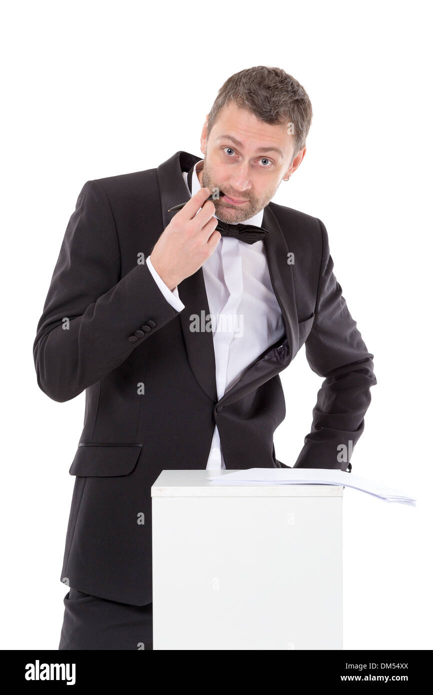 Elegante uomo di mezza età in un bow tie e tuta in piedi in un piedistallo di completare un modulo mettendo in pausa per leggere il documento con una penna Foto Stock