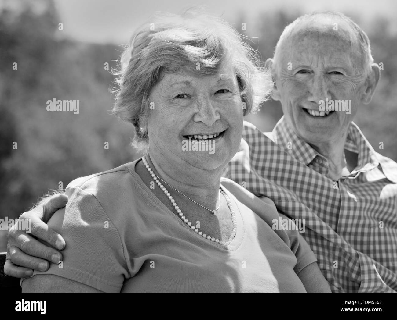 Coppia matura seduta e sorridente all'esterno nella luce del sole Foto Stock