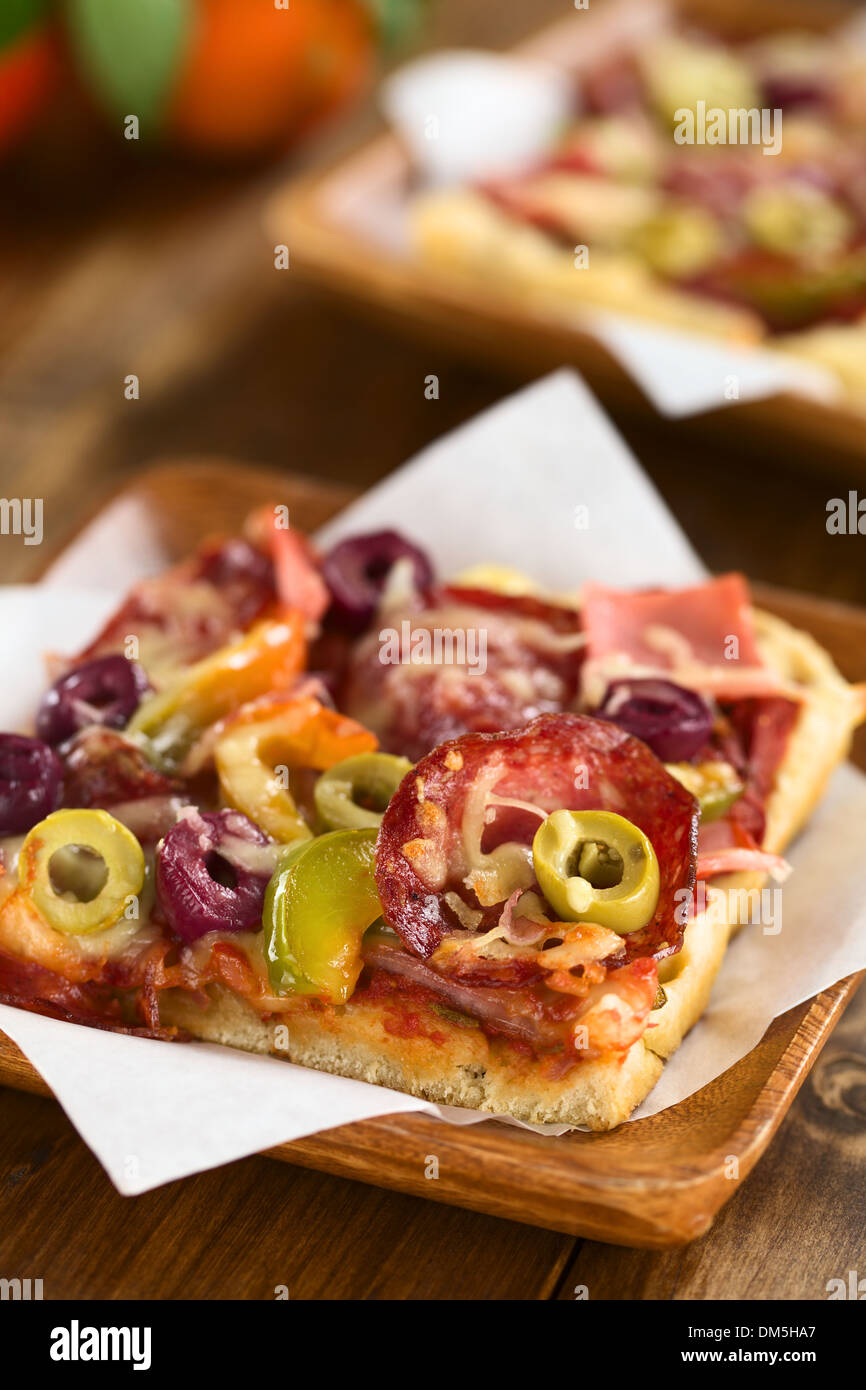 Freschi Fatti in casa pezzo di pizza con salsa di pomodoro, prosciutto, salame, olive, peperone e formaggio in cima, servita sulla carta a sandwich Foto Stock