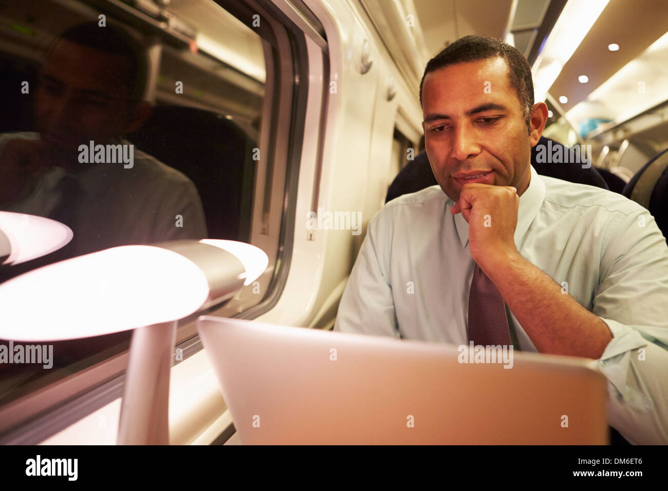 Imprenditore il pendolarismo per lavorare sul treno e utilizzando computer portatile durante la notte Foto Stock