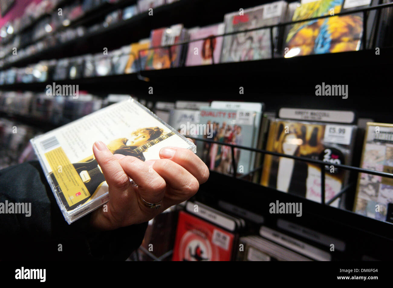 Donna manicotto di lettura delle note e via elenco sul retro di un CD nella parte anteriore del rack di CD musicali in un record shop. Foto Stock