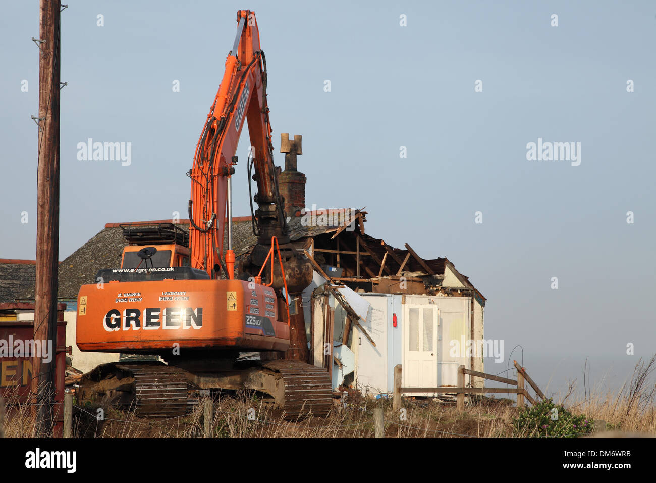 Un escavatore cingolato per demolizione Doosan Solar 225 LC-V con un gancio/benna per demolizione per impieghi gravosi che demolisce un edificio a Norfolk nel Regno Unito. Escavatore idraulico cingolato arancione che utilizza una benna per demolizione per abbattere una struttura industriale bassa, con macerie e detriti che cadono a terra. Macchinari pesanti per l'edilizia in fase di ristrutturazione sotto un cielo nuvoloso. Foto Stock