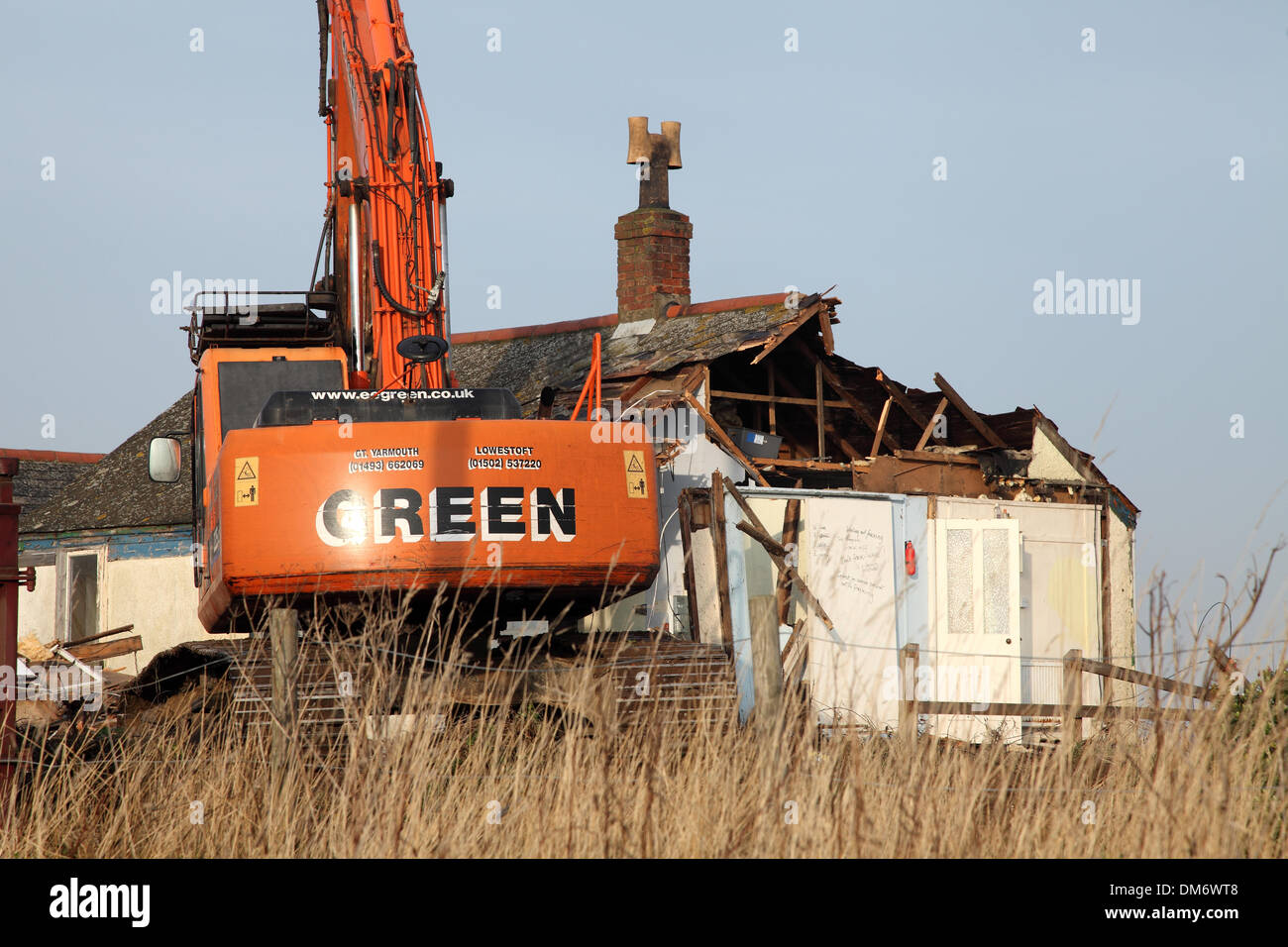Un escavatore cingolato per demolizione Doosan Solar 225 LC-V con un gancio/benna per demolizione per impieghi gravosi che demolisce un edificio a Norfolk nel Regno Unito. Escavatore idraulico cingolato arancione che utilizza una benna per demolizione per abbattere una struttura industriale bassa, con macerie e detriti che cadono a terra. Macchinari pesanti per l'edilizia in fase di ristrutturazione sotto un cielo nuvoloso. Foto Stock