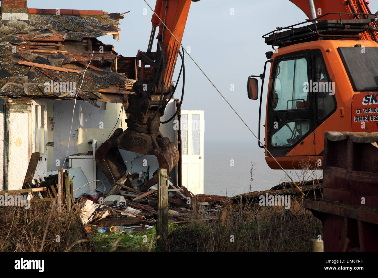 Un escavatore cingolato per demolizione Doosan Solar 225 LC-V con un gancio/benna per demolizione per impieghi gravosi che demolisce un edificio a Norfolk nel Regno Unito. Escavatore idraulico cingolato arancione che utilizza una benna per demolizione per abbattere una struttura industriale bassa, con macerie e detriti che cadono a terra. Macchinari pesanti per l'edilizia in fase di ristrutturazione sotto un cielo nuvoloso. Foto Stock