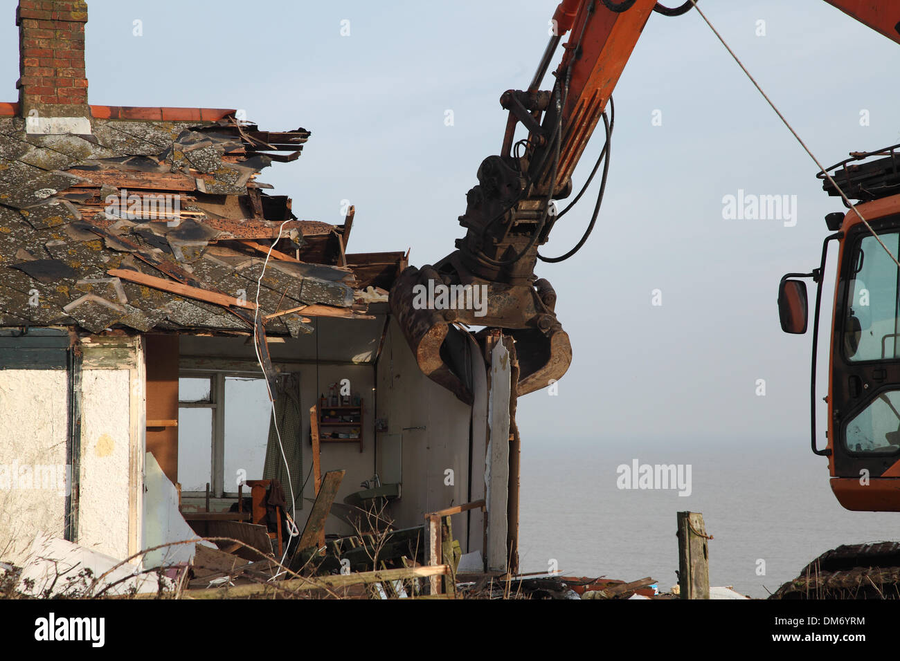 Un escavatore cingolato per demolizione Doosan Solar 225 LC-V con un gancio/benna per demolizione per impieghi gravosi che demolisce un edificio a Norfolk nel Regno Unito. Escavatore idraulico cingolato arancione che utilizza una benna per demolizione per abbattere una struttura industriale bassa, con macerie e detriti che cadono a terra. Macchinari pesanti per l'edilizia in fase di ristrutturazione sotto un cielo nuvoloso. Foto Stock
