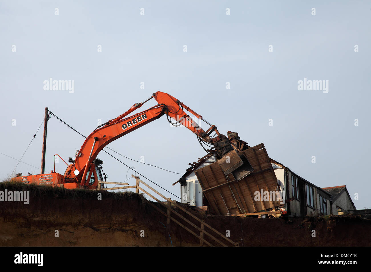 Un escavatore cingolato per demolizione Doosan Solar 225 LC-V con un gancio/benna per demolizione per impieghi gravosi che demolisce un edificio a Norfolk nel Regno Unito. Escavatore idraulico cingolato arancione che utilizza una benna per demolizione per abbattere una struttura industriale bassa, con macerie e detriti che cadono a terra. Macchinari pesanti per l'edilizia in fase di ristrutturazione sotto un cielo nuvoloso. Foto Stock
