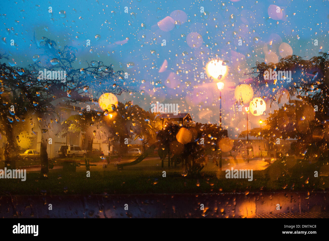 Guardando attraverso le gocce di pioggia su una finestra per la strada fuori all'alba con lampioni svasatura attraverso il sensore di pioggia Foto Stock