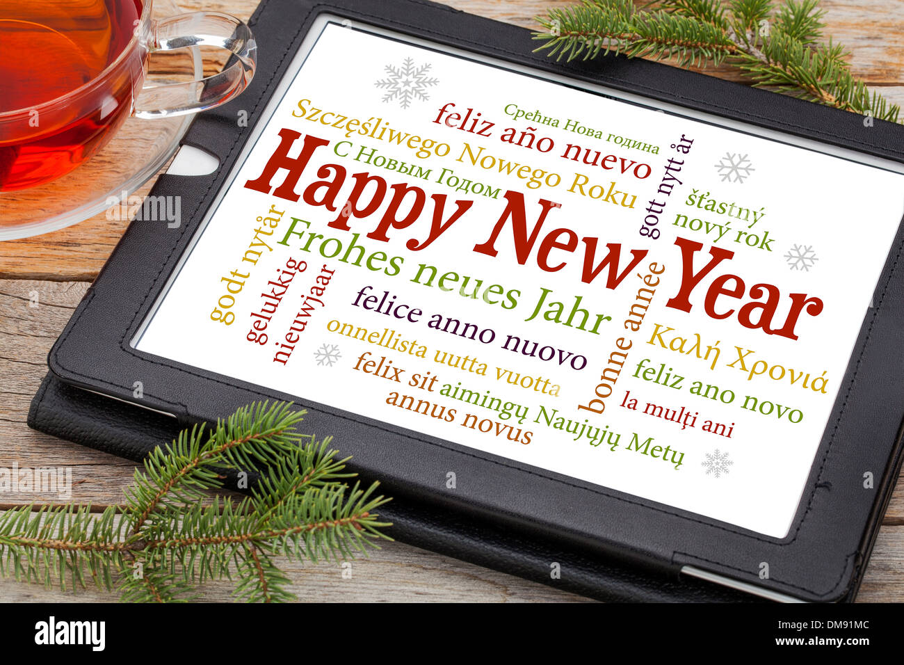 Felice Anno Nuovo in diverse lingue su una tavoletta digitale con una tazza di tè e rametti di abete rosso Foto Stock