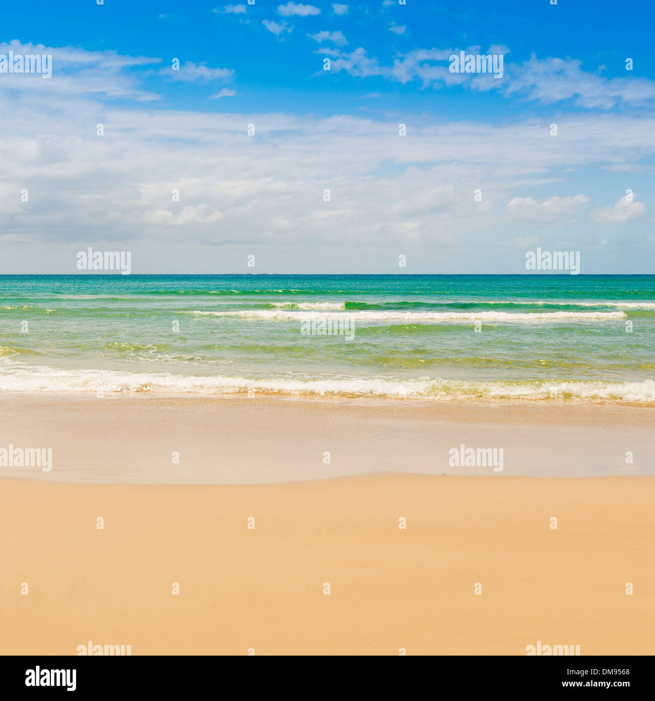 Spiaggia con cielo blu e blu acqua lambiscono la sabbia Foto Stock