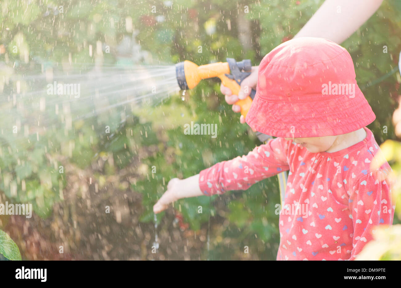 Stile di vita estate scena. Bambina giocando con il genitore nel giardino, sensazione di acqua dagli sprinkler Foto Stock
