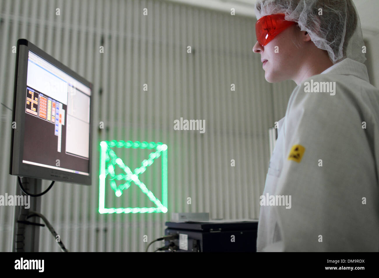 Una donna in piedi con cleanroom cappotto è di lavorare in un laboratorio per la tecnologia e i dispositivi di controllo di un dispositivo calcolatore per un laser Foto Stock