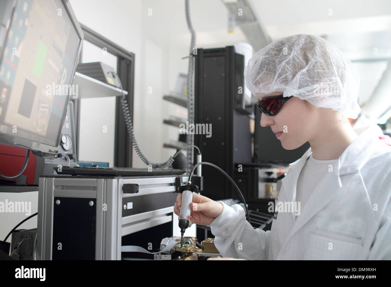 Una donna in piedi con cleanroom cappotto è di lavorare in un laboratorio per i dispositivi dotati di tecnologia e cluing un dispositivo per un laser Foto Stock