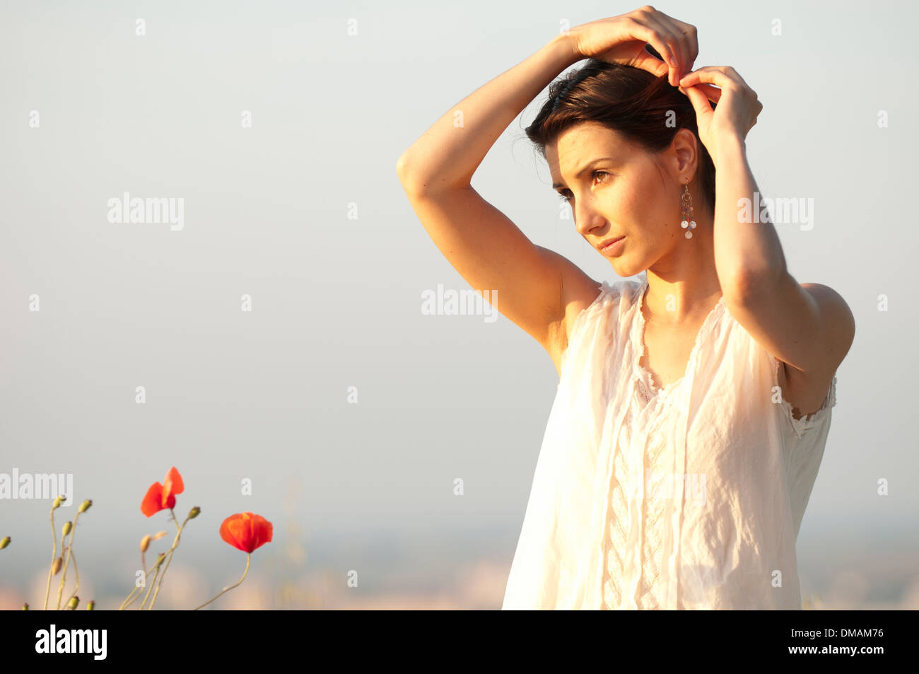 Giovane donna in abito sorge al tramonto in un cornfield con papaveri Foto Stock