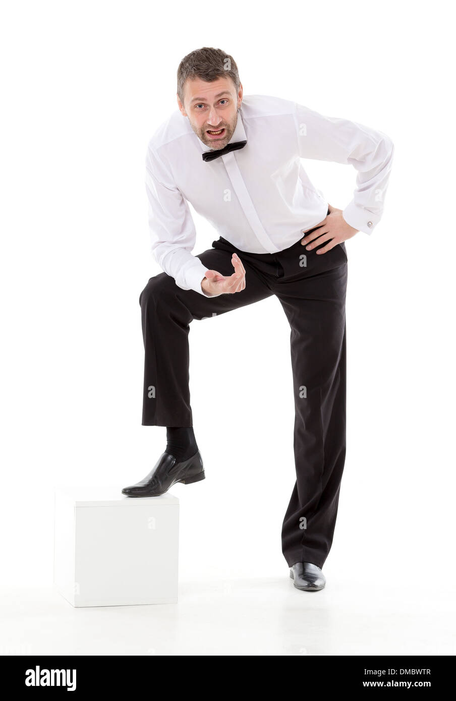 Uomo elegante in un bow tie appoggiato su di un piedistallo di basso a parlare con la telecamera mentre guardando verso l'alto e gesti con le mani Foto Stock