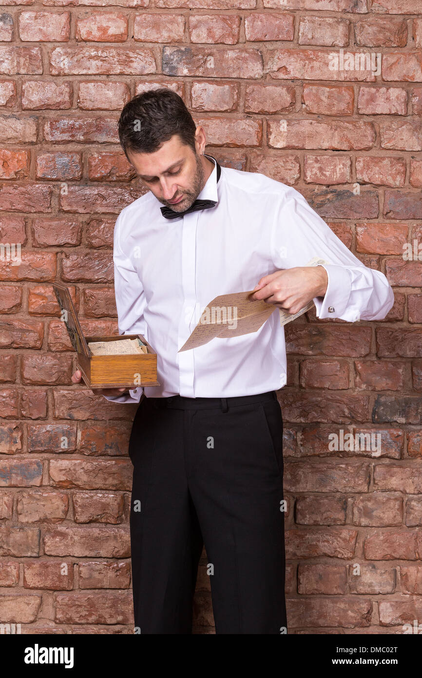 Uomo in piedi la lettura di un vecchio documento da una scatola di legno che sta tenendo in mano mentre in piedi di fronte a un muro di mattoni Foto Stock